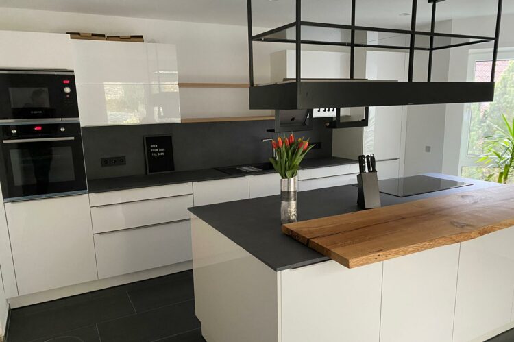 Küche Hochglanz weiß mit Arbeitsplatte aus Naturstein schwarz und Theke aus Echtholz massiv.
