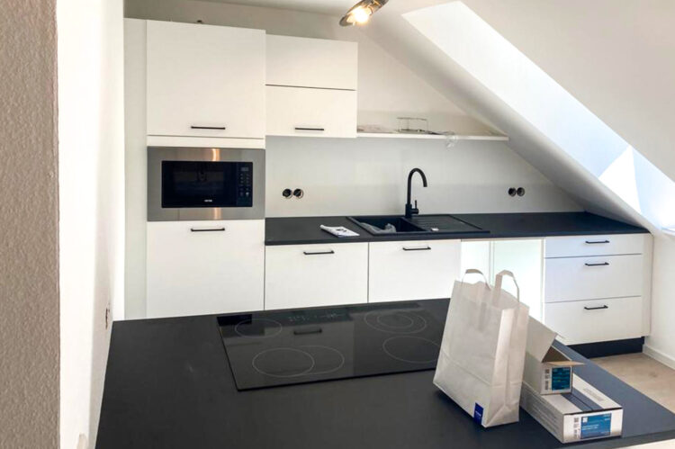 Weiße Küche mit Kochinsel von Expressküchen passend in Dachschräge mit schwarzer Arbeitsplatte