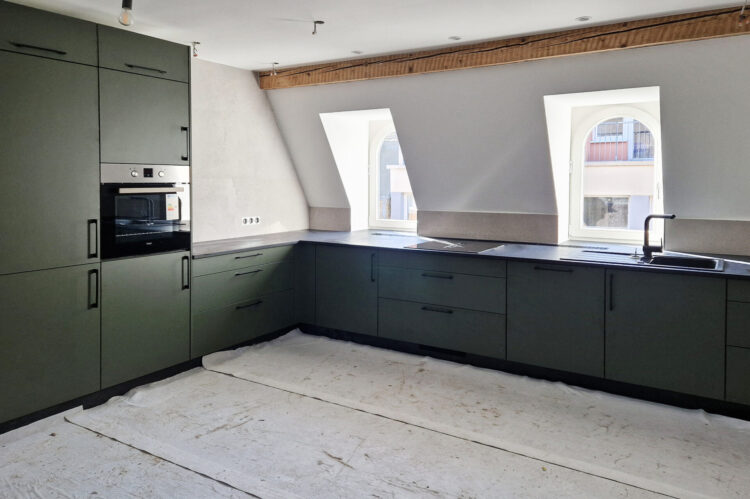 Häcker Küche olivgrün mit schwarzen Griffen, eingebautem Kühlschrank, schwarzem Spülbecken mit schwarzer Armatur und Kochfeld mit Muldenlüfter